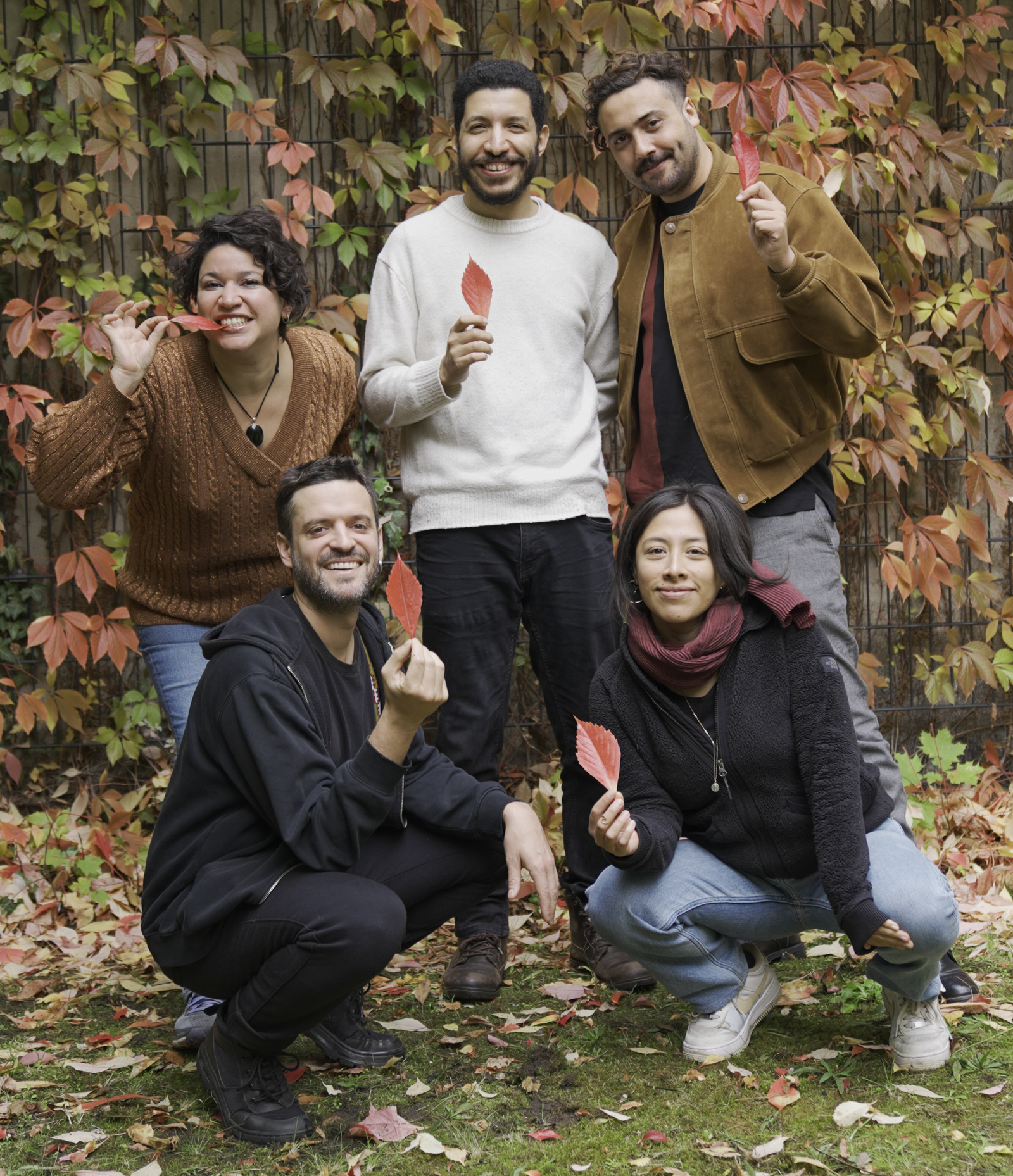 This image features the five members of Red Leaves Films gathered in an autumn setting, with fallen leaves on the ground and each holding a red leaf in their hand.